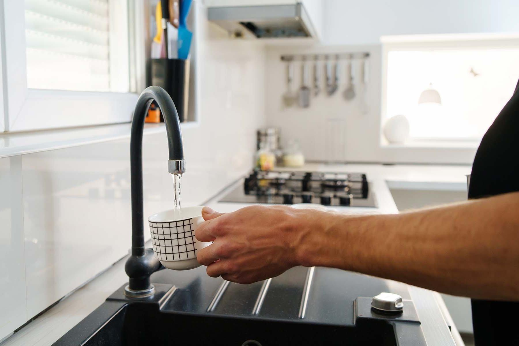 A person fills a patterned cup with water from a kitchen tap